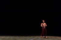 a male dancer standing on a stage in front of a dark background